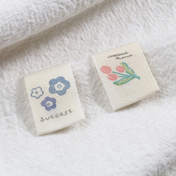 100PCs Flower Printed Brige Labels Миещи се детски дрехи Чанти Облекло Основни етикети Ръчно изработени памучни тъкани етикети Шевни аксесоари