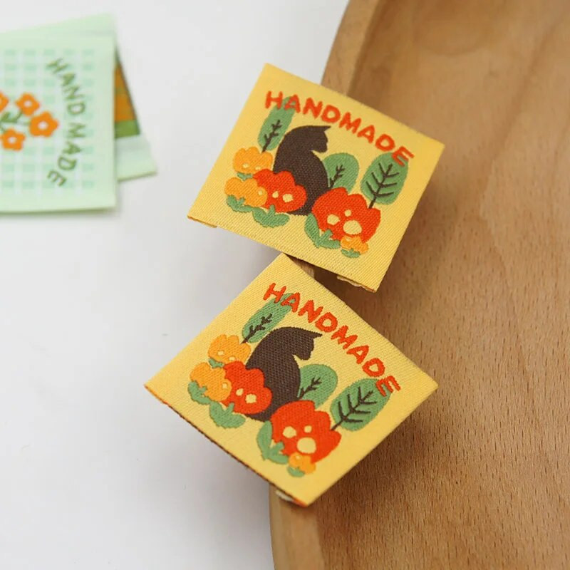 Ar rokām darināta auduma etiķete noliktavā, jauks pleds mazs zieds, kaķu izšuvumi, austa etiķete, aksesuāri, šūšana, krāsaina etiķete